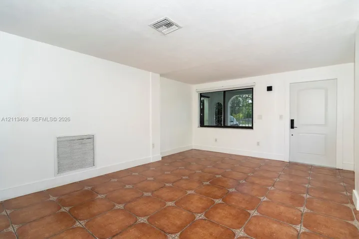 Interior room featuring large-format terra cotta tile flooring, white walls, a single-panel door, and a black-framed window