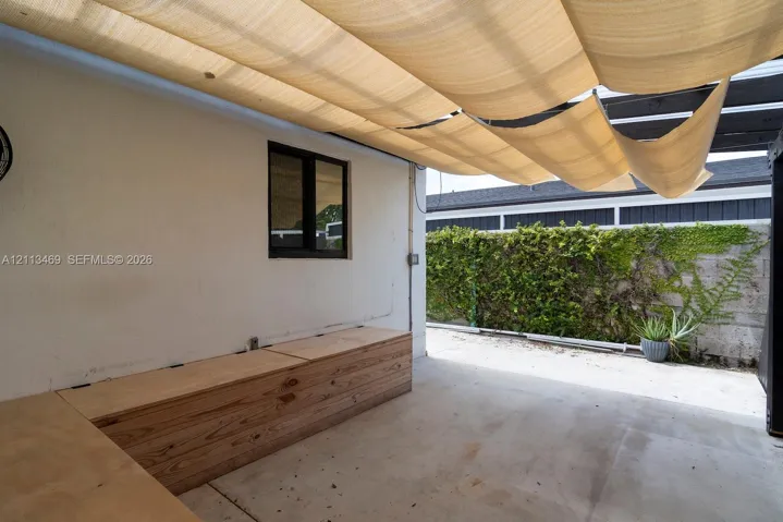 Covered patio featuring a retractable fabric canopy, concrete flooring, built-in natural wood cabinetry, and a masonry perimeter wall with climbing vegetation