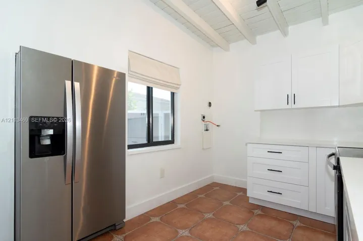 Kitchen featuring white shaker-style cabinetry, matte black hardware, stainless steel side-by-side refrigerator, tile flooring, and exposed white-painted ceiling beams