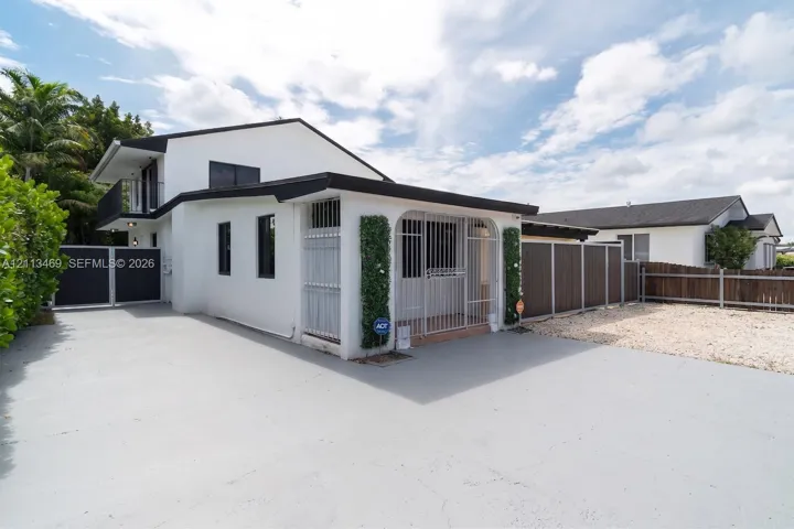Two-story exterior featuring white stucco finish, flat roofline, metal security screening, covered entryway with arched opening, and concrete driveway