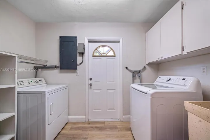 Laundry area featuring wood-finish flooring, white upper wall-mounted cabinetry, integrated shelving, and a utility sink