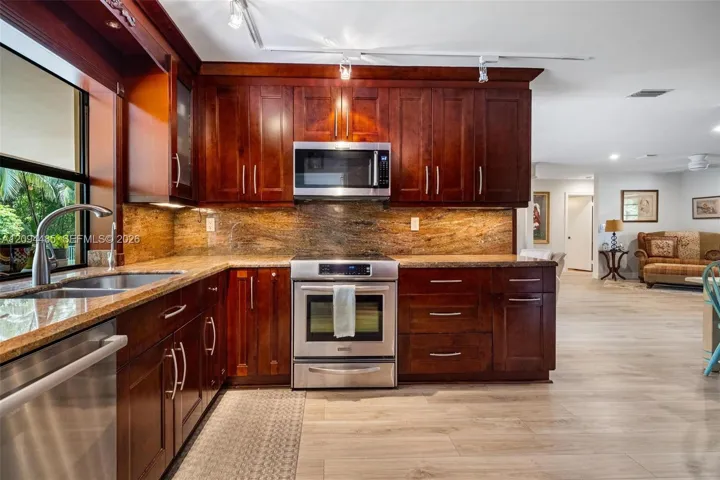 Kitchen featuring dark wood cabinetry, stainless steel appliances, stone countertops, stone backsplash, and track lighting