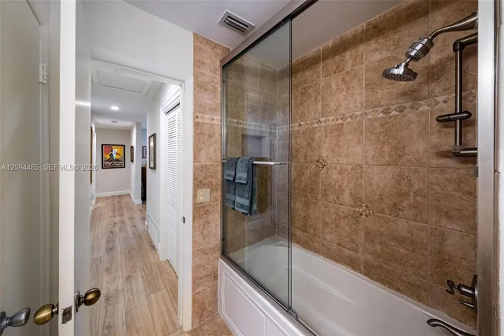 Shower-tub combination featuring floor-to-ceiling tile surround with decorative inlay, glass sliding shower door, recessed wall niche, and metal hardware