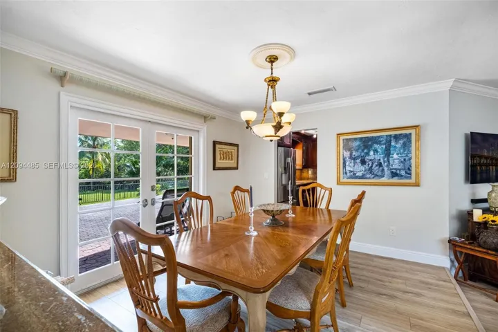 Dining area featuring wood-finish flooring, crown molding, a central multi-light chandelier with a decorative medallion, and double glass-paned doors with exterior access