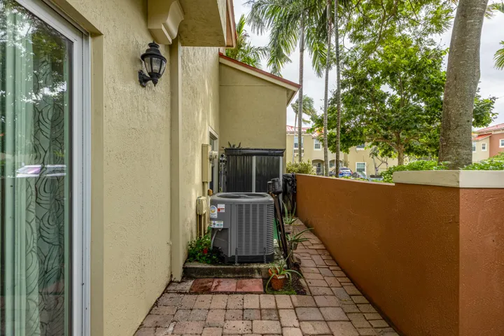 Exterior side passage featuring paver hardscaping, a stucco privacy wall, and an attached outdoor light fixture