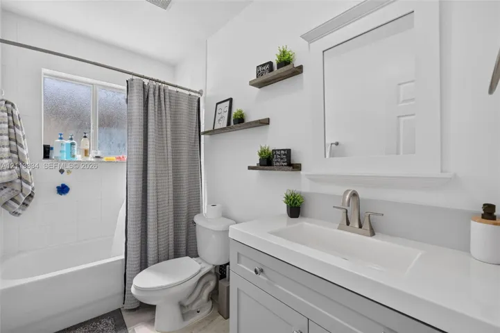 Bathroom featuring a gray vanity with an integrated rectangular sink, brushed nickel faucet, white-tiled shower surround, and three wood-finish wall-mounted shelves