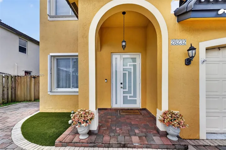 Stucco exterior featuring a recessed entry with an arched portico, decorative glass panel entry door, paver porch flooring, and exterior carriage lighting