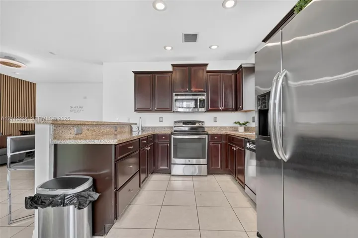Kitchen featuring dark-toned wood cabinetry, stone countertops, stainless steel appliances, and ceramic tile flooring