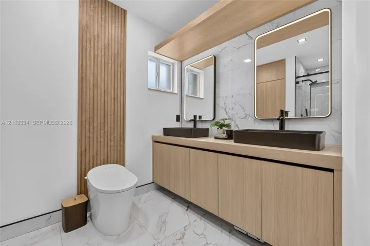 Floating vanity featuring wood-finish cabinetry, dual rectangular vessel sinks, matte black faucets, integrated LED-lit mirrors, and floor-to-ceiling wood slat wall detailing
