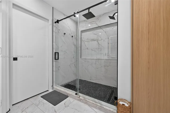 Walk-in shower featuring large-format wall tiling, a sliding glass door, matte black hardware, a rainfall showerhead, and a recessed wall niche