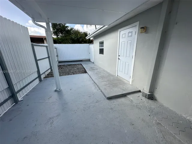 Covered patio featuring concrete flooring, white corrugated metal fencing, and an exterior door with integrated lighting