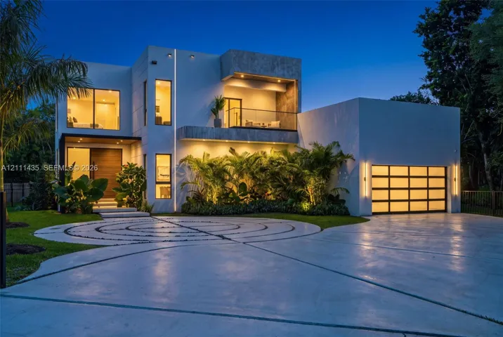 Modern architectural exterior featuring smooth stucco siding, an upper-level glass-railed balcony, a multi-pane glass garage door, and a geometric concrete driveway