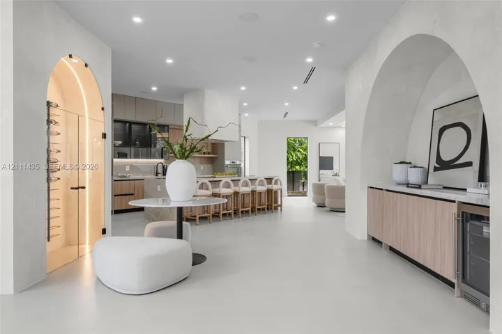 Open-concept floor plan featuring arched architectural entryways, a climate-controlled glass wine cellar, custom light wood cabinetry, and recessed lighting