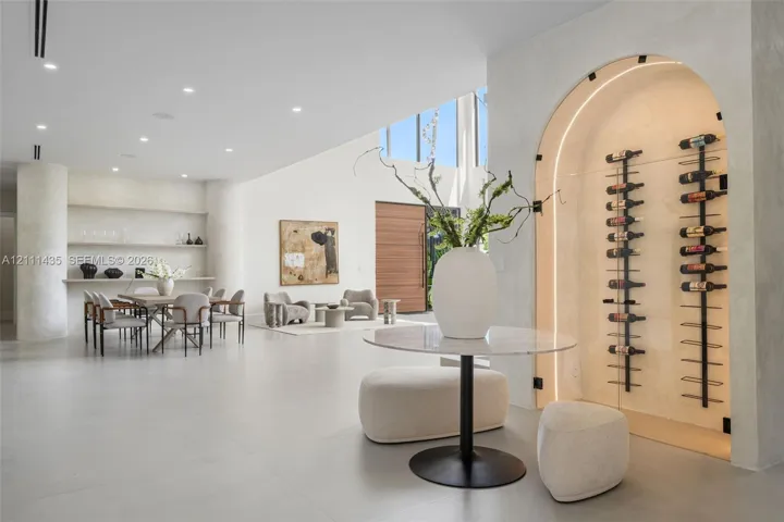 Arched, climate-controlled glass wine display with integrated accent lighting, built-in shelving, smooth plaster wall finishes, recessed ceiling lighting, and large-format tile flooring