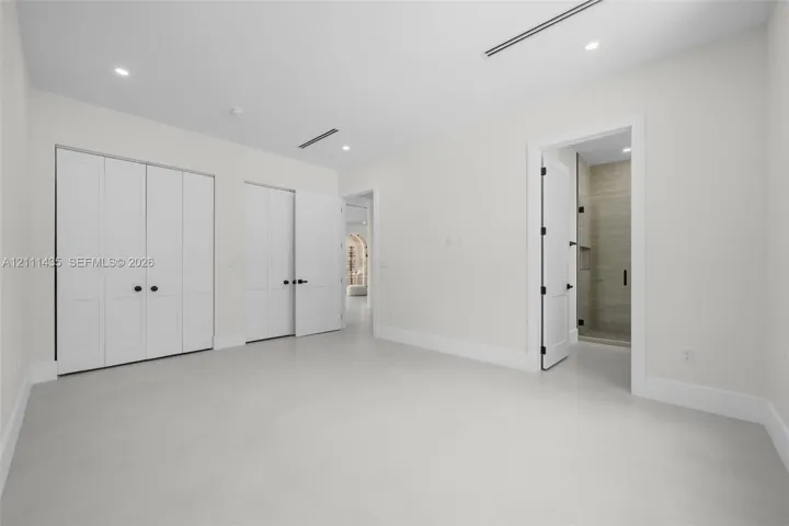 Room featuring smooth flooring, recessed lighting, double-door closet cabinetry, and a doorway revealing a tiled shower enclosure