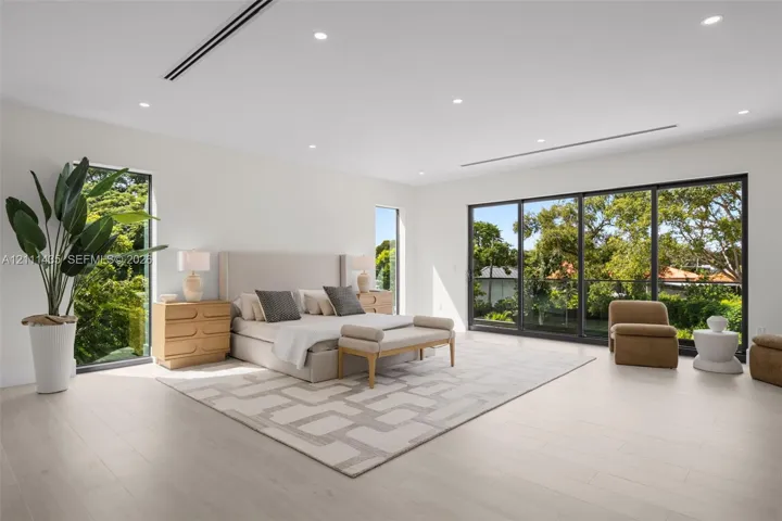 Spacious interior featuring light-toned wood-finish flooring, recessed lighting, full-height windows, and floor-to-ceiling sliding glass doors with dark metal frames