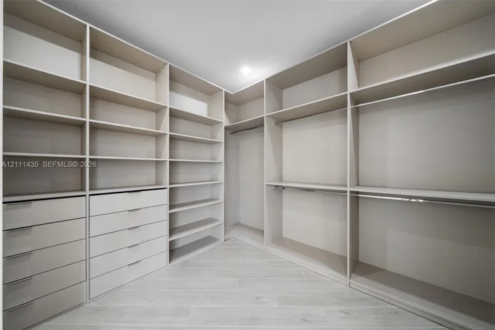 Walk-in closet featuring extensive built-in shelving, integrated multi-drawer cabinetry, dual-level hanging rods, and light-toned tile flooring