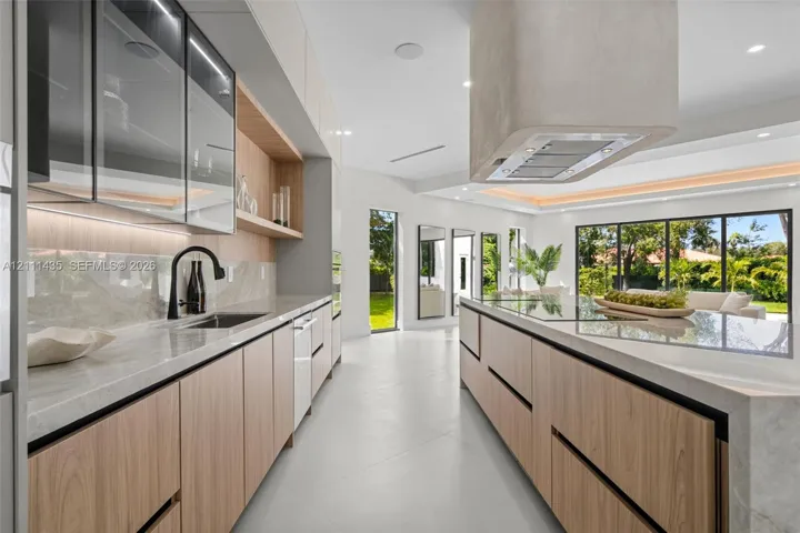 Kitchen featuring light wood-finish cabinetry, stone countertops, integrated under-cabinet lighting, a contemporary ceiling-mounted range hood, and large-format tile flooring
