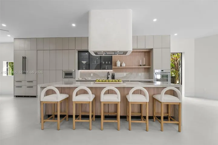 Kitchen featuring a waterfall-edge island, custom cabinetry, integrated high-end appliances, a stone-finish backsplash, and a floating range hood