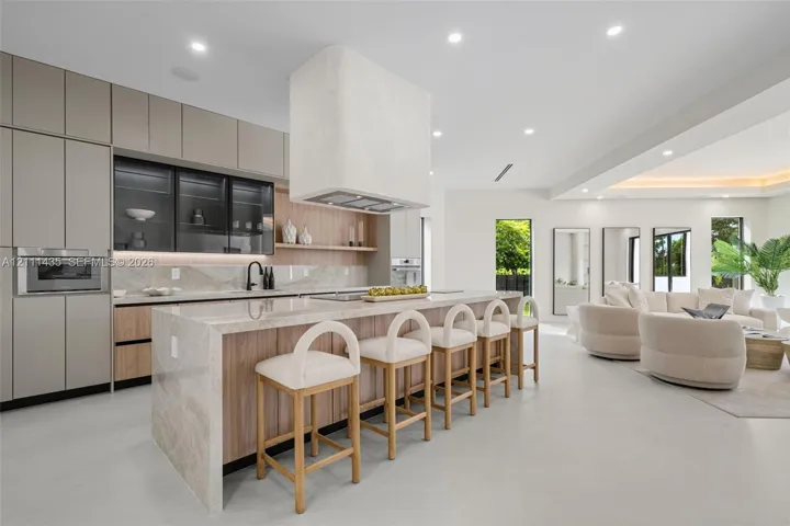 Modern kitchen featuring matte-finish cabinetry, a waterfall-edge stone island, integrated oven and microwave, recessed lighting, and a custom plaster range hood