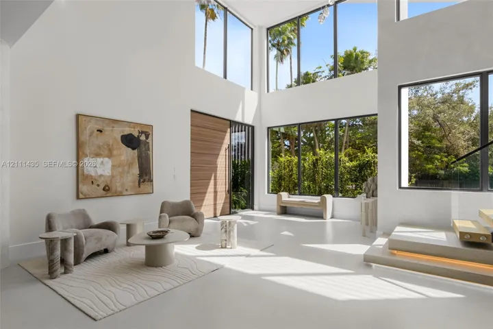 Double-height living area featuring floor-to-ceiling windows, polished concrete flooring, a natural wood entry door, and a floating staircase with integrated lighting
