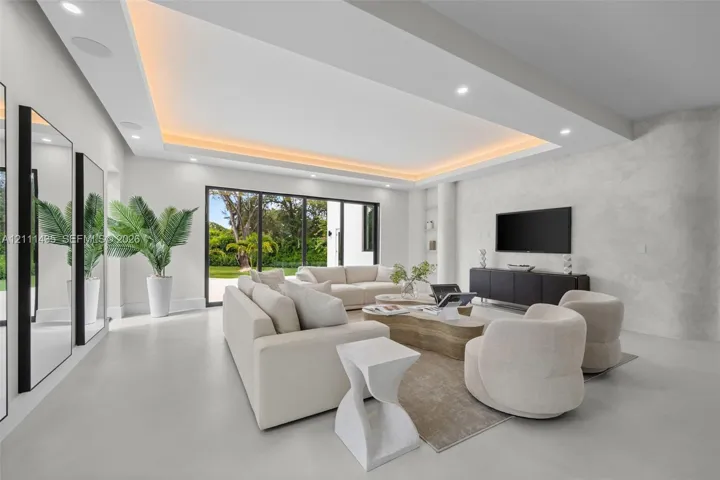 Living area featuring a coffered ceiling with integrated cove lighting, recessed ceiling lights, a textured stone-finish accent wall, and multi-panel floor-to-ceiling glass sliding doors