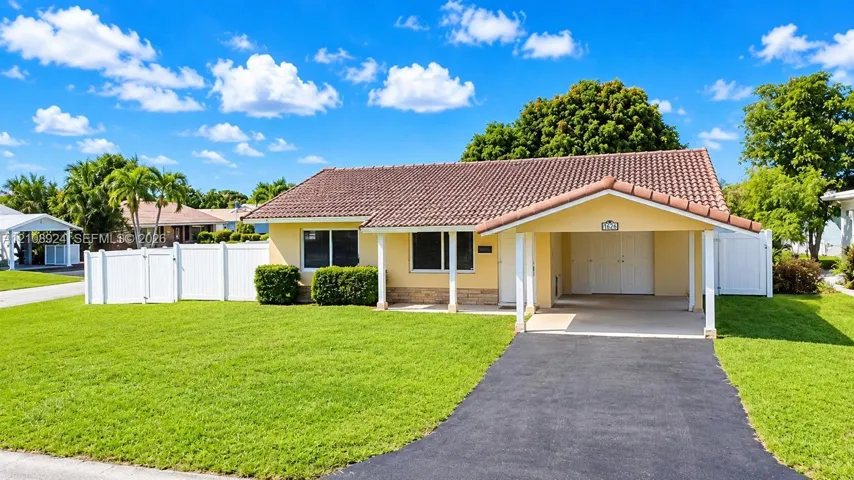 Single-story residence featuring a tile roof, covered carport, asphalt driveway, and white perimeter fencing