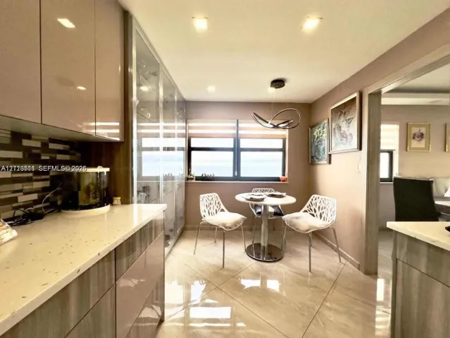 High-gloss cabinetry, stone-finish countertops, geometric glass-tile backsplash, floor-to-ceiling built-in display cabinetry, and polished large-format tile flooring