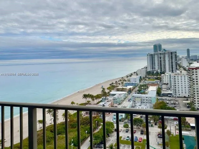 Elevated balcony featuring metal railings and a panoramic perspective of the coastline, sandy beach, and ocean