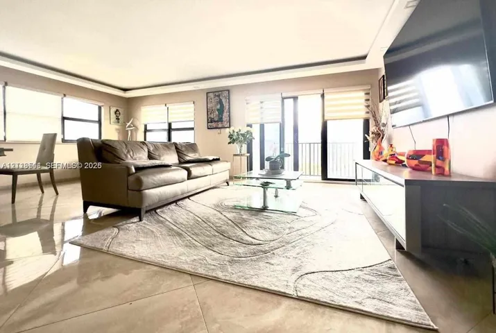 Living space featuring large-format tile flooring, recessed tray ceiling, multiple floor-to-ceiling windows with integrated roller shades, and sliding glass doors with balcony access