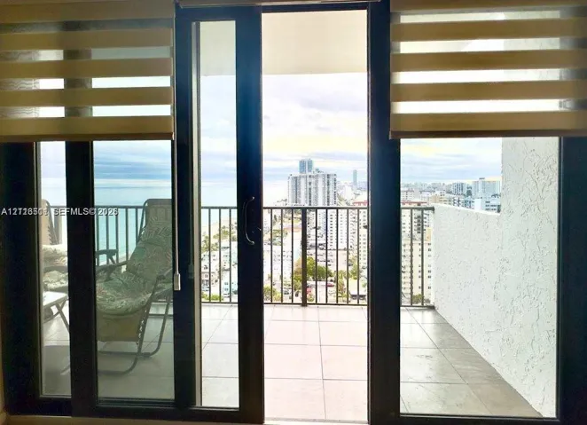 Floor-to-ceiling glass sliding doors opening to a private balcony with tile flooring, metal railings, and panoramic coastal and urban scenery