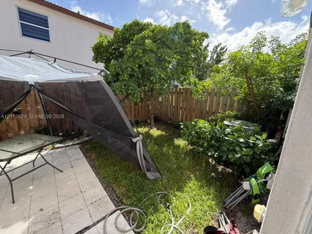 Backyard area featuring a stone tile patio, privacy wood fencing, mature trees, and established shrubs