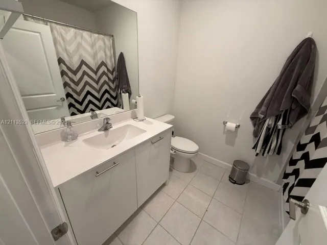 Bathroom featuring a white vanity cabinet with a solid surface countertop, an integrated basin, a full-width wall mirror, and neutral floor tile