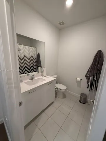 Bathroom featuring a white vanity cabinet with a stone-composite countertop, an integrated rectangular sink, large-format neutral floor tile, and a wall-mounted mirror