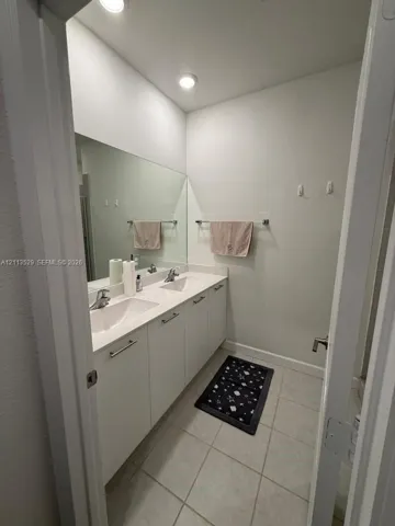 Dual-sink vanity with white cabinetry, light-toned countertop, integrated rectangular basins, polished chrome faucets, and a full-width wall mirror