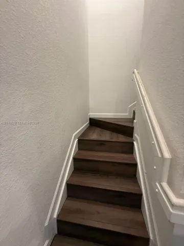 Staircase featuring wood-finish treads, white paneled walls, and a matching white handrail