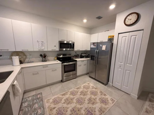 Kitchen featuring flat-panel white cabinetry, light-toned stone-finish countertops, stainless steel appliances, tile flooring, and a floor-to-ceiling built-in pantry with bi-fold doors