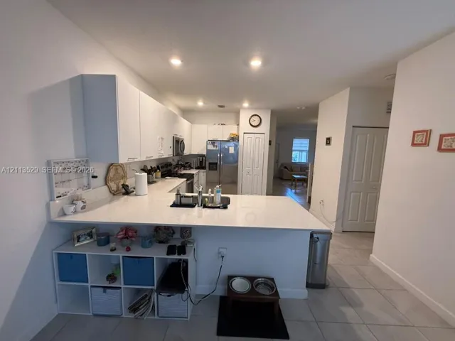 Kitchen featuring a peninsula with a stone-finish countertop, white cabinetry, stainless steel appliances, recessed lighting, and tile flooring