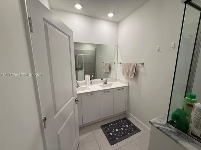 Bathroom featuring a double-sink vanity with white cabinetry and a solid-surface countertop, full-width wall mirror, recessed lighting, and tile flooring