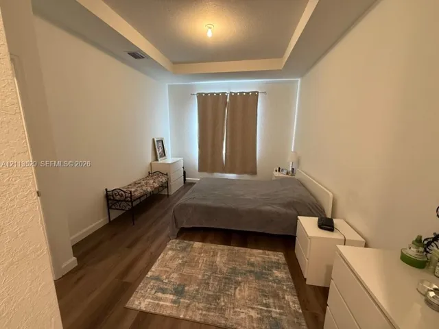 Room featuring a tray ceiling, recessed center panel, and wood-finish flooring