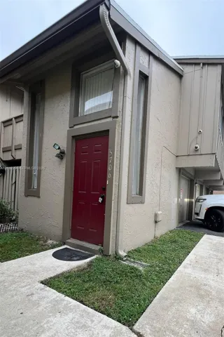 Exterior facade featuring a stucco finish, accent vertical windows, a red paneled entry door, and integrated outdoor lighting fixtures