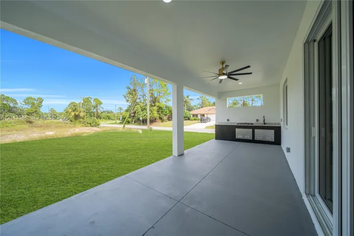 Covered patio featuring concrete flooring, a ceiling fan with integrated lighting, and an outdoor kitchen area with a built-in cooktop, sink, and cabinetry