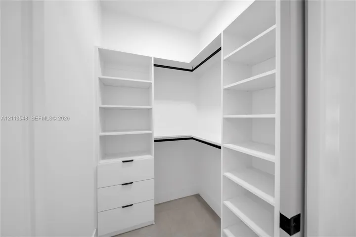 Custom walk-in closet featuring white built-in shelving, a three-drawer storage unit, matte black hardware, and hanging rods