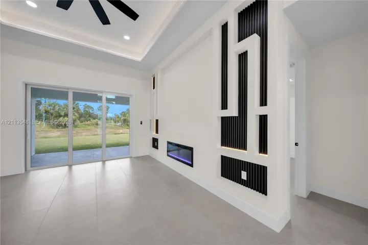 Tray ceiling with recessed lighting, large-format tile flooring, wall-mounted electric fireplace, custom geometric wall accent with vertical slat detailing, and multi-panel sliding glass doors