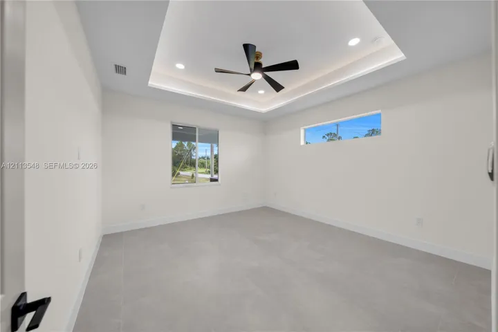 Tray ceiling featuring recessed lighting and a central ceiling fan, expansive tile flooring, and horizontal transom window
