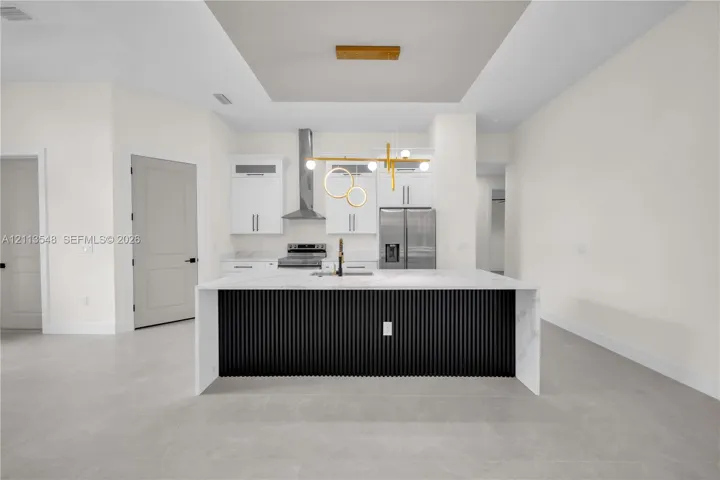 Kitchen featuring white cabinetry, center island with stone countertop and fluted black detailing, stainless steel appliances, and modern gold-tone pendant lighting