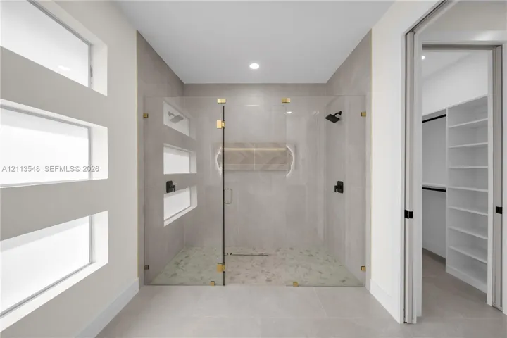 Walk-in shower featuring glass paneling, gold-tone hardware, recessed lighting, stone-tiled flooring, and a decorative herringbone inlay