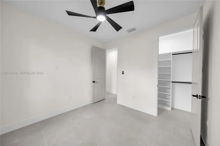 Neutral-toned tile flooring, contemporary multi-blade ceiling fan, and built-in closet shelving with hanging rods