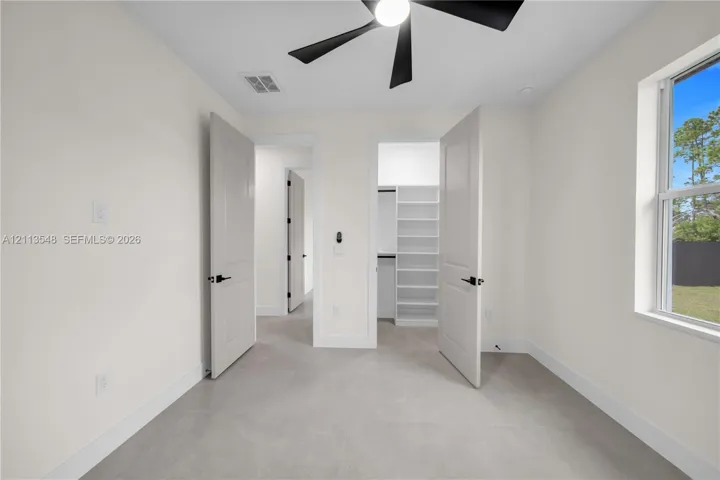Room featuring neutral-toned tile flooring, built-in shelving, matte black hardware, a ceiling fan, and a single-hung window
