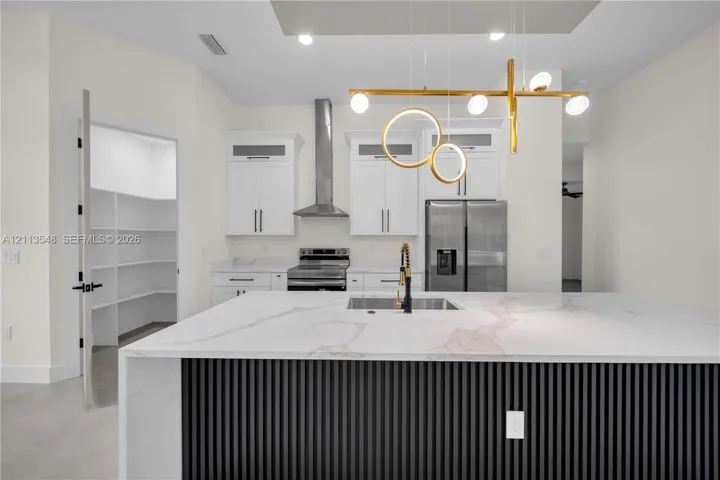 Kitchen island featuring a waterfall-edge stone countertop, decorative vertical-slatted base, and integrated sink with a gold-tone faucet